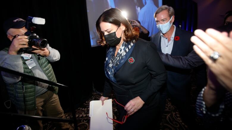 A woman wearing a face mask walks past cheering supporters and a photographer.