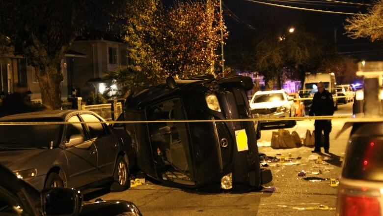 A car is on its side, surrounded by debris