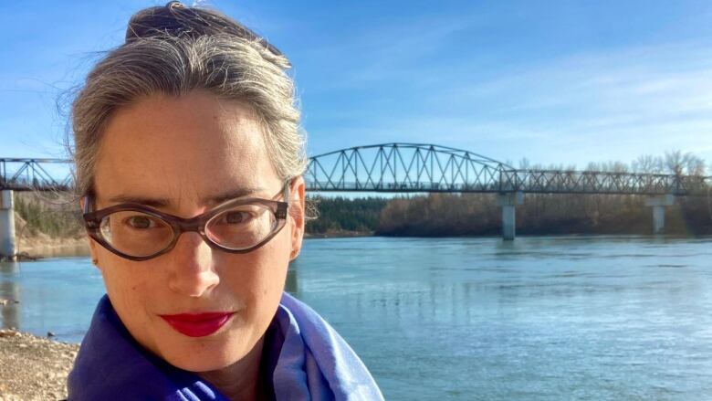 A woman with her hair pulled back wearing glasses and with a river and bridge in the background