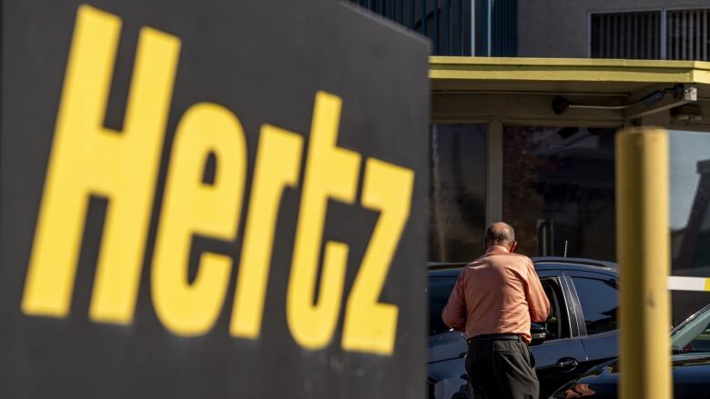 A large sign is picture at a Hertz car rental lot, showing the company's logo.