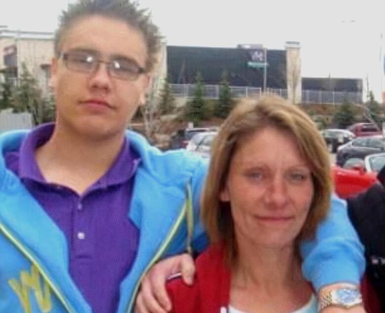 A young man stands with his arm around a woman. 