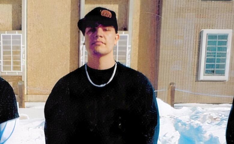 A man stands in front of a prison with his hands folded in front of him. 