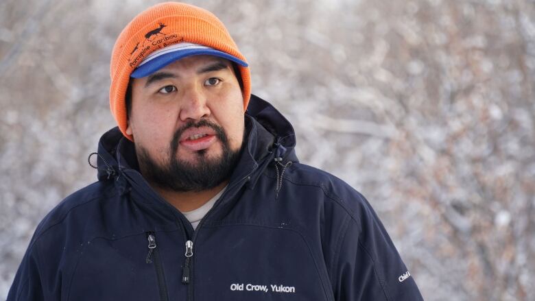 A man with a winter coat and hat is visible in the winter woods.