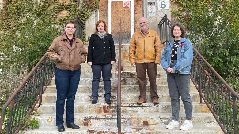 four people stand on the steps of a building