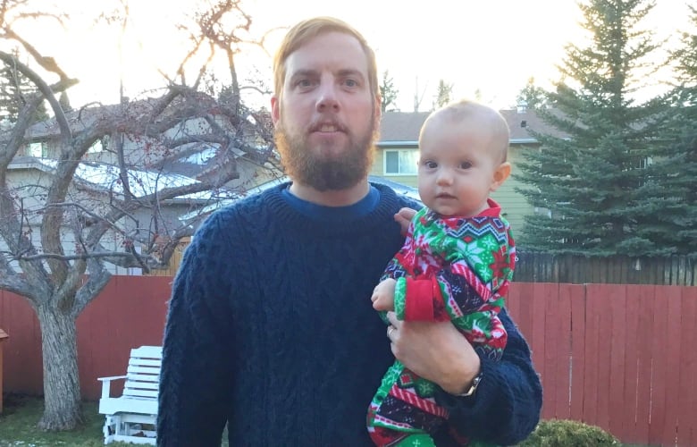 A bearded man stands with baby daughter