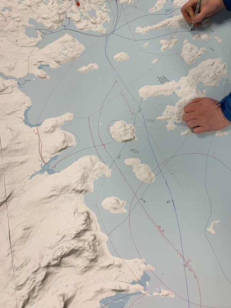 Hands move over a map of coastal Labrador. There are a series of lines drawn with marker across the map.