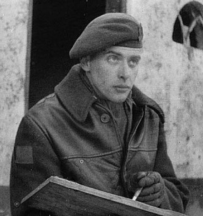 A man in a beret draws in a sketchbook in a black and white photo.