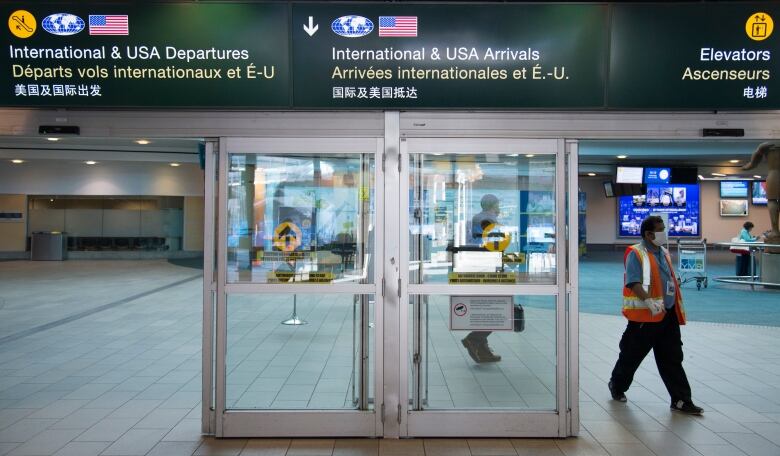 An airport worker in a high-vis vest walks past an airport entrance at Vancouver International Airport.