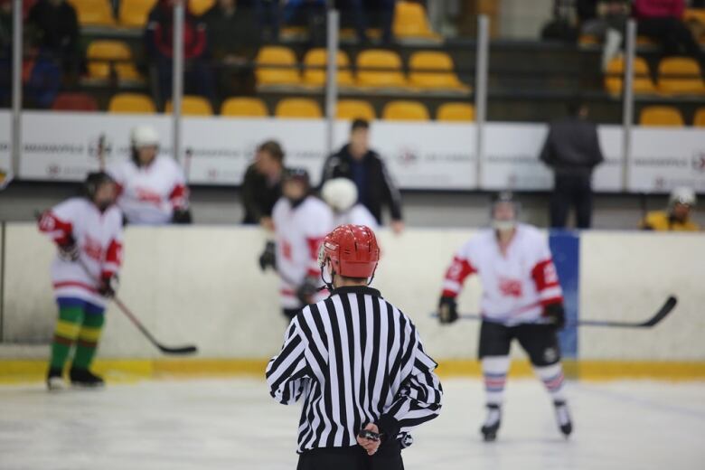 A hockey referee is pictured from the back as they look on at a bench.