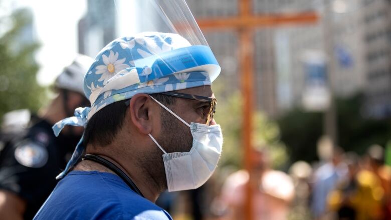 A healthcare professional watches as  demonstrators gather outside Toronto General Hospital, on September 13, 2021, to protest against COVID-19 vaccines, COVID-19 vaccine passports and COVID-19 related restrictions.