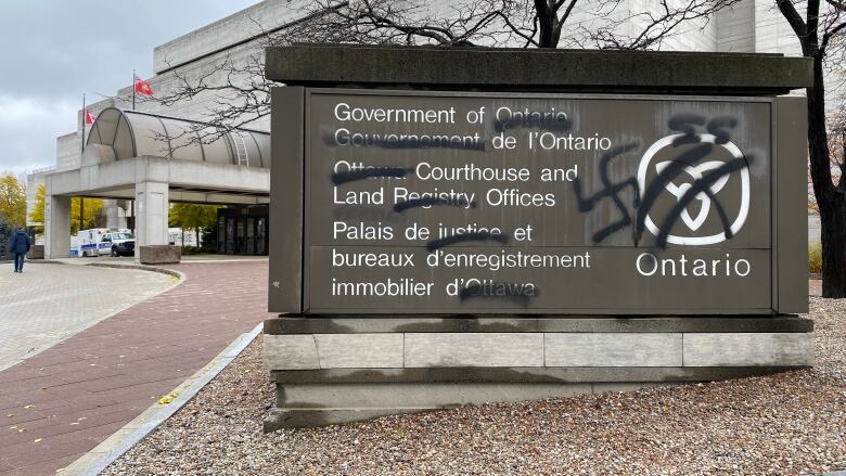 A sign for a provincial courthouse is vandalized with a swastika.