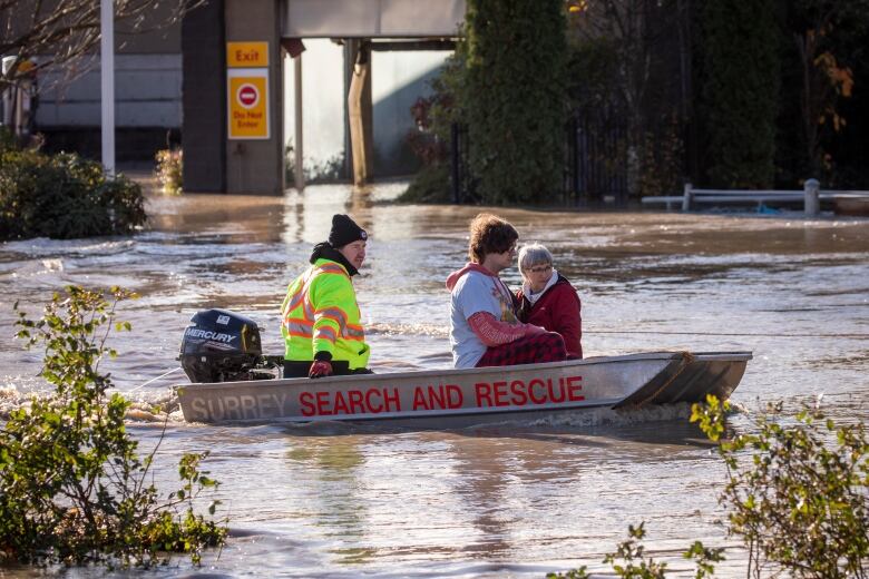 Three people in a search and rescue boat floating along a flooded road