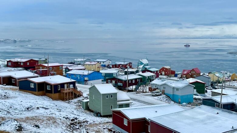 Rows of houses sit on snow with water in the background.