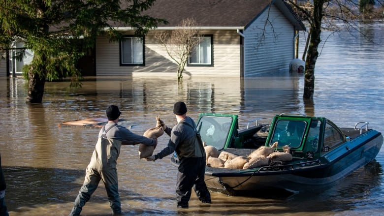 Two men load sandbags off a boat while standing in knee deep water 