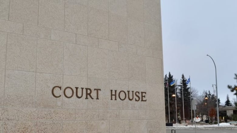 The gold-coloured words 'Court House' hang on a stone building wall. There are trees and flag poles in the distant background.