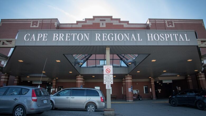 The canopy at the front entrance of the Cape Breton Regional Hospital is shown, with several cars parked underneath. 