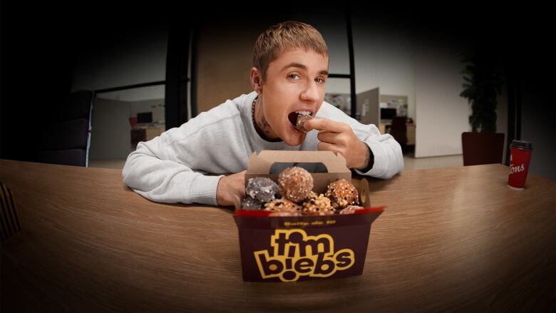 A man poses with a box of doughnuts. He holds one to his mouth. 