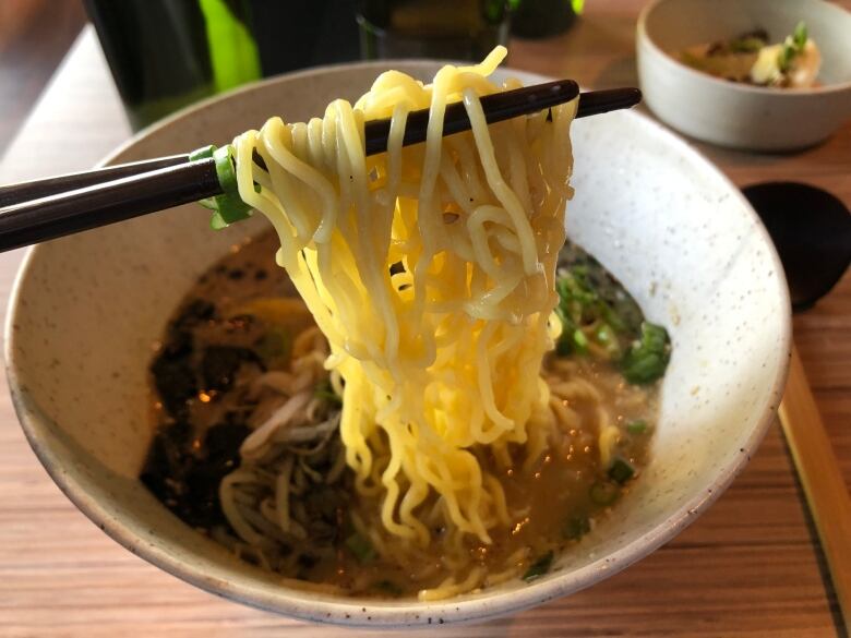 Chopsticks hold noodles over a bowl of broth.