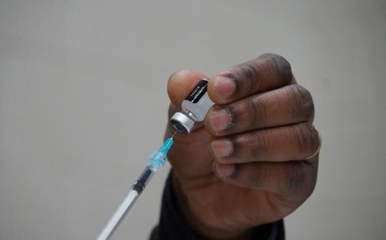 A close-up of a hand holding a vaccine vial as a needle is filled from it.