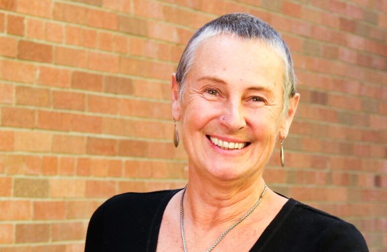 Woman with short hair smiles in front of a brown brick wall in a black top.