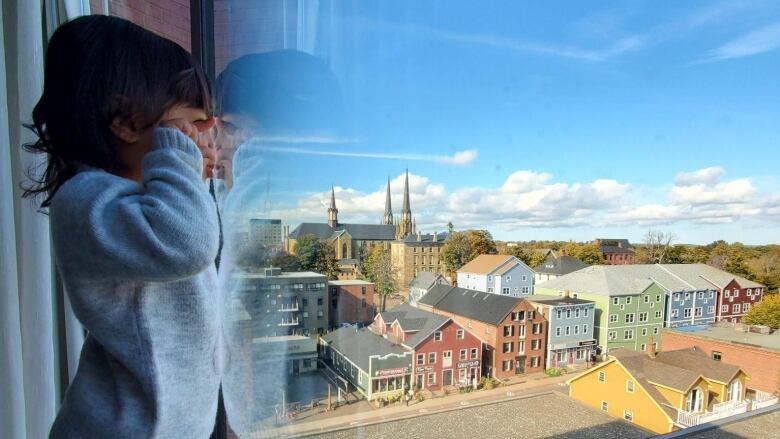 A small child stands on a window sill looking outside