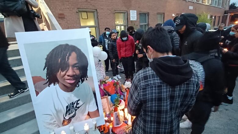 people bow their heads in front of candles and a picture of a Black teen who was murdered