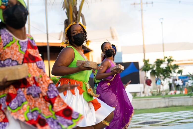 Women in colourful clothes dance in the streets.