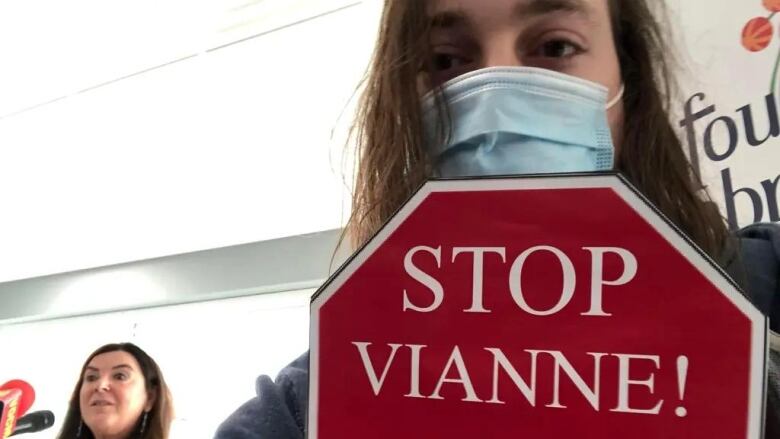 A man with long hair, wearing a non-medical mask, holds a stop sign that says 