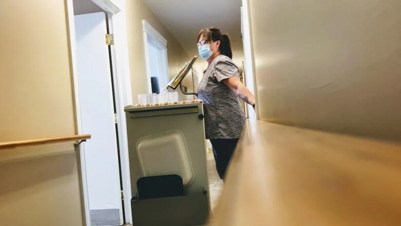 A nursing home worker in a mask wheeling a cart with medication cups on it