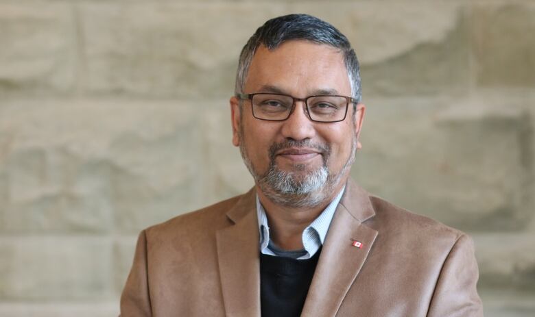 A man in a brown suit stands for a photo.