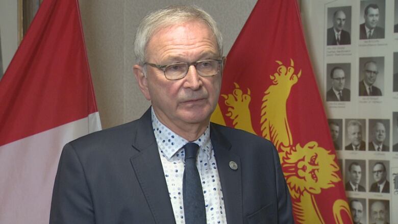 Premier standing in front of Canadian and New Brunswick flags.