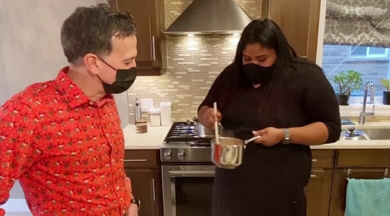 A chef holds a pot while speaking with a man (food columnist) in a home kitchen