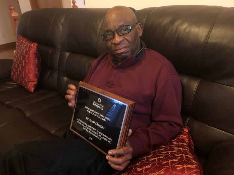 A man sits on a couch holding a plaque