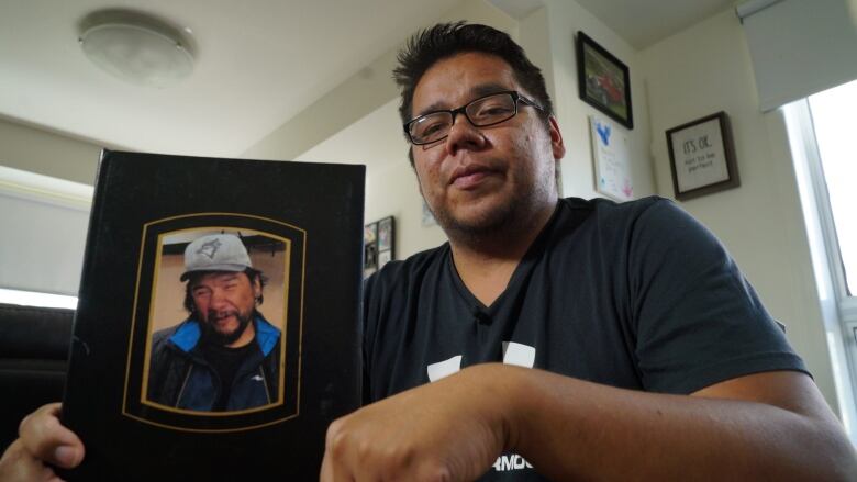 A man wearing glasses holding a framed photo of a man.