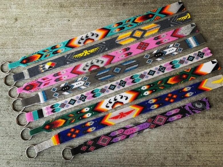 Eight multicoloured beaded lanyards are seen againt a concrete backdrop.