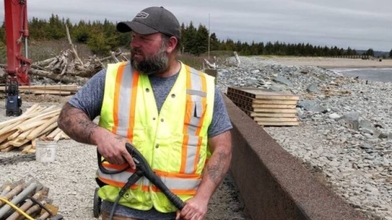 A man wearing a safety vest is shown at a construction site next to a beach.