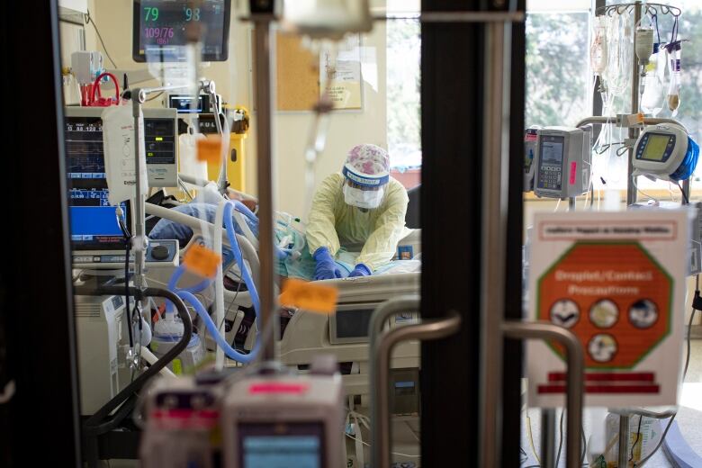 An ICU nurse is seen caring for a patient in a hospital bed through the window of a door.