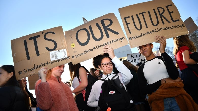 Young demonstrators hold cardboard signs that, when connected, say 