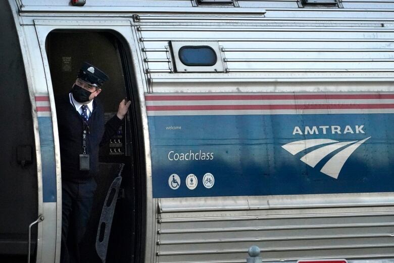 A man wearing a mask stands in the door of a train marked 'Amtrak'.