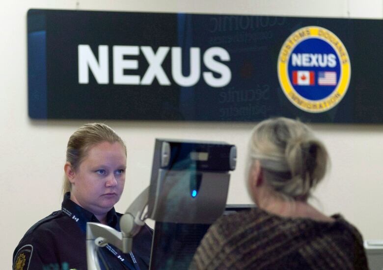 A woman border officer faces a woman passenger at an office in an airport.