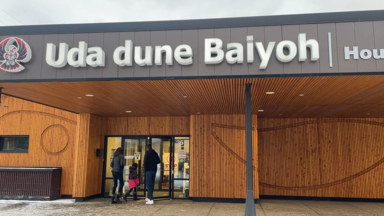 Two adults and child walk into a building that has signage reading 'Uda dune Baiyoh.'