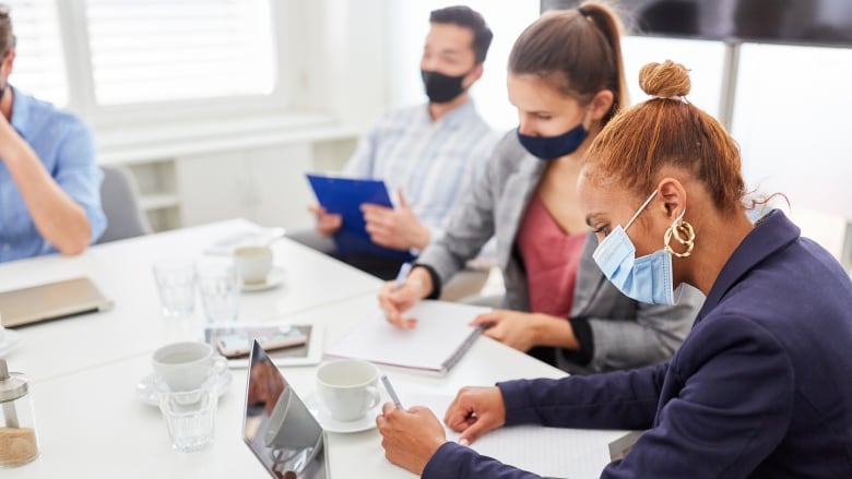 People wearing masks sit around a workplace table. 