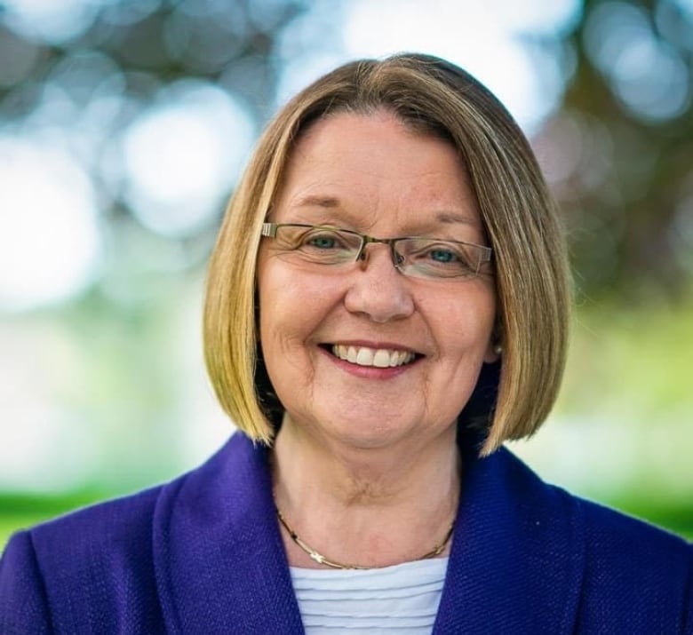 A smiling woman with short hair and glasses wearing a blue blazer. 