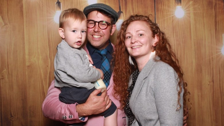 A woman and man holding a toddler smile at the camera