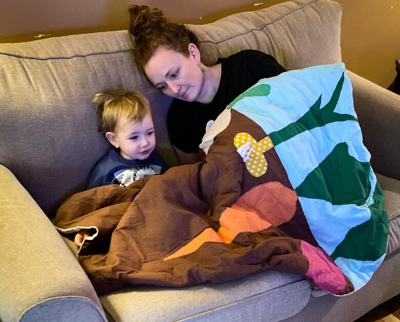 A woman lies on a couch with a small child