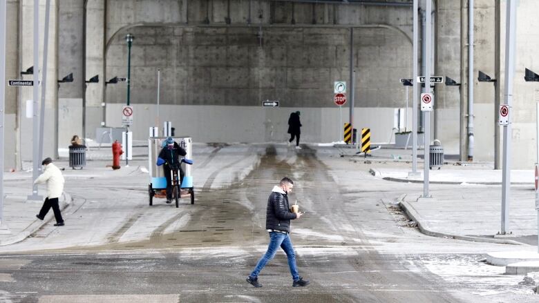  person holding an iced coffee walks across a street, while a courier on a bike cycles through