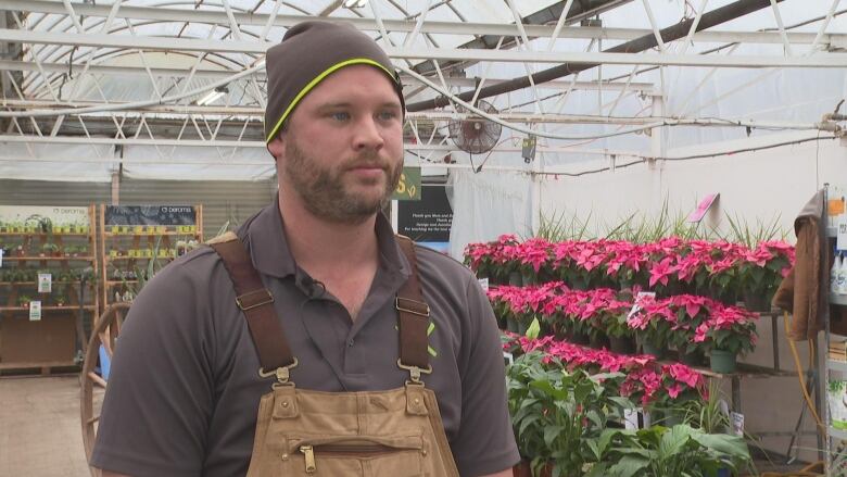 man in a greenhouse, behind are plants