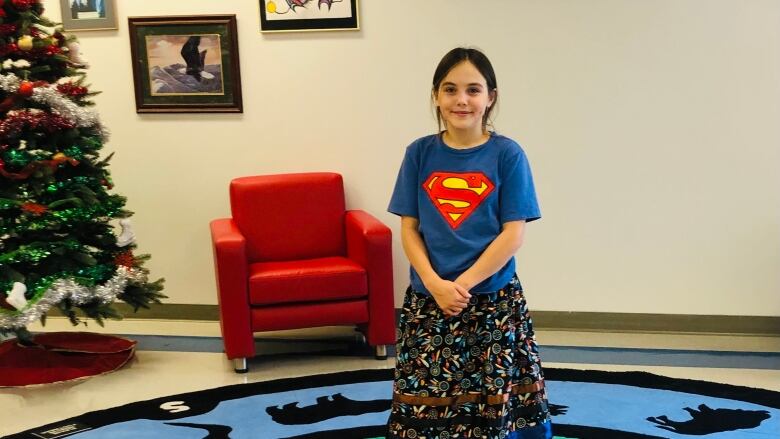 A young girl poses wearing a ribbon skirt.