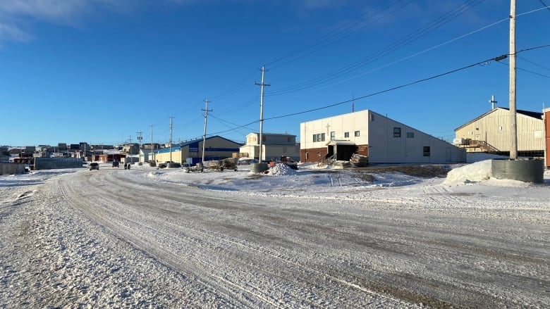 a wide snowy road is flanked by buildings on the right side