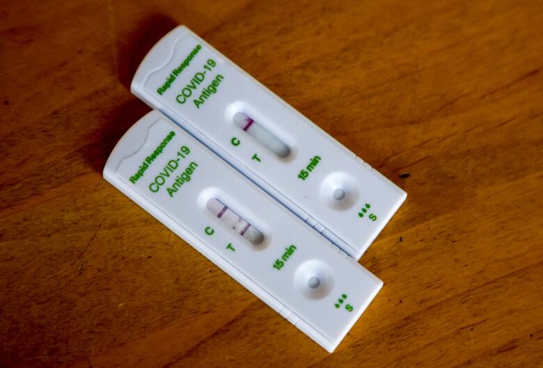 Two rapid COVID-19 tests, one with a positive result and the other with a negative result, are shown.